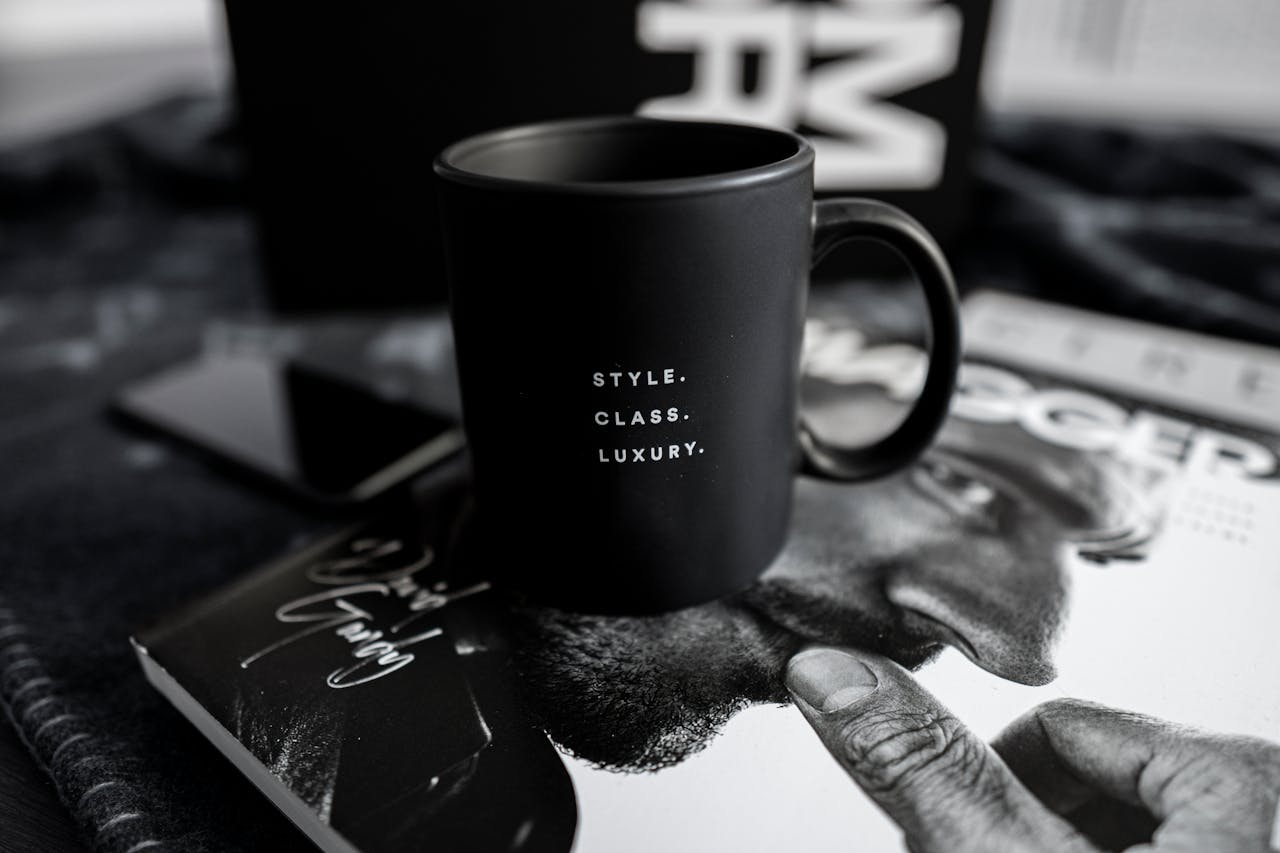 about-01 A stylish black mug with text sits on a luxury magazine, presenting an elegant and modern lifestyle setting indoors.